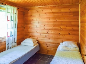 A small, wooden cabin room with two single beds, a window with curtains, and a tiled floor. - Nuppulanranta 14 by Interhome (Kuhmoinen)