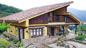 Ein zweistöckiges Haus mit Stein Fundament, Holzbalkon und einer Terrasse mit Topfpflanzen und Gartenmöbeln.