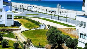 A coastal area with a road leading to a beach, modern buildings, and a clear view of the sea. - Residence Cite Jardin 4065 (Martil)