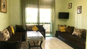 A living room with two dark-colored sofas, a small table, and a window with curtains. - Residence Cite Jardin 4065 (Martil)