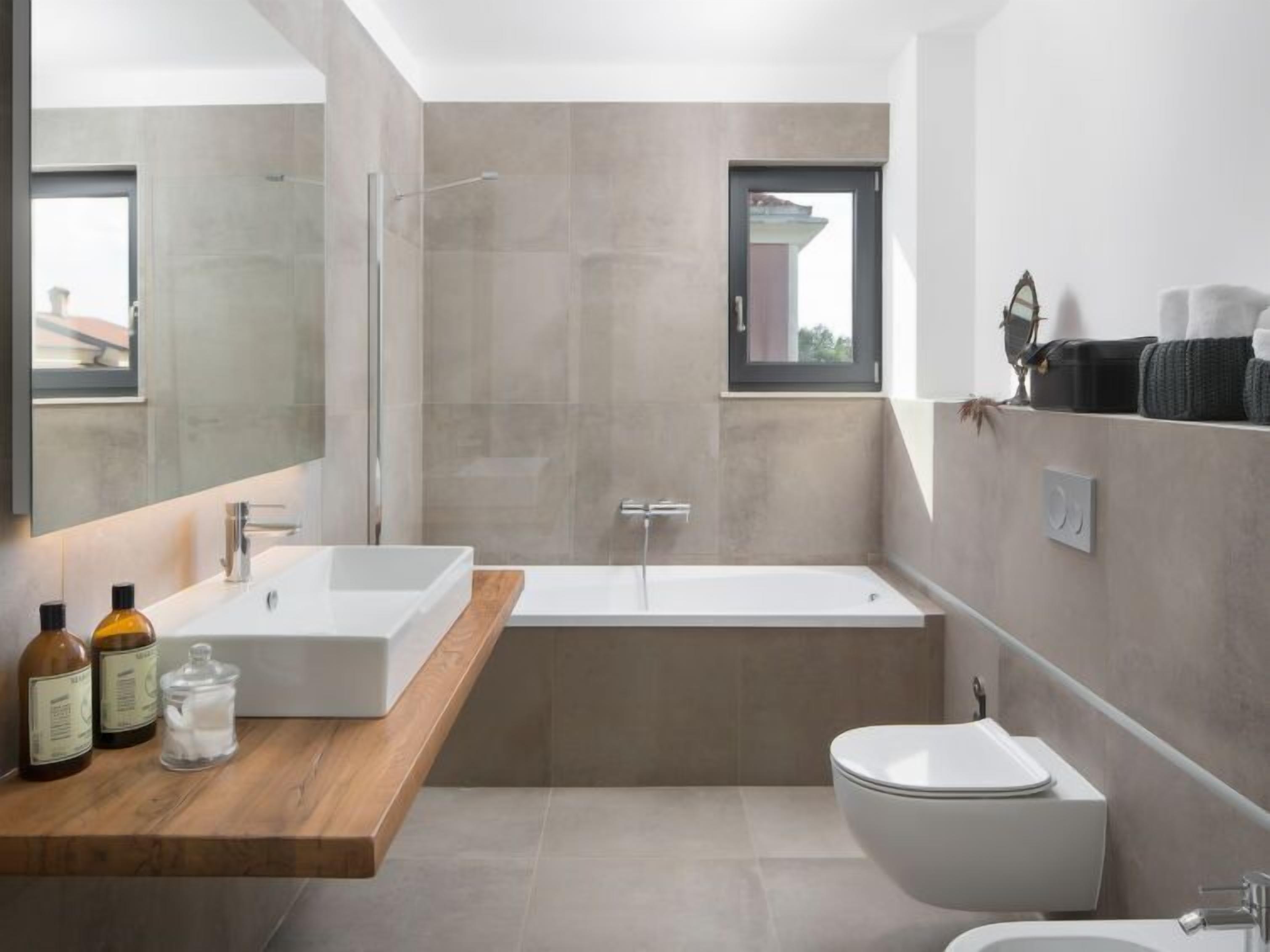 Ein modernes Badezimmer mit einem großen Spiegel, einer freistehenden Badewanne, einem weißen Waschbecken und einer Toilette.