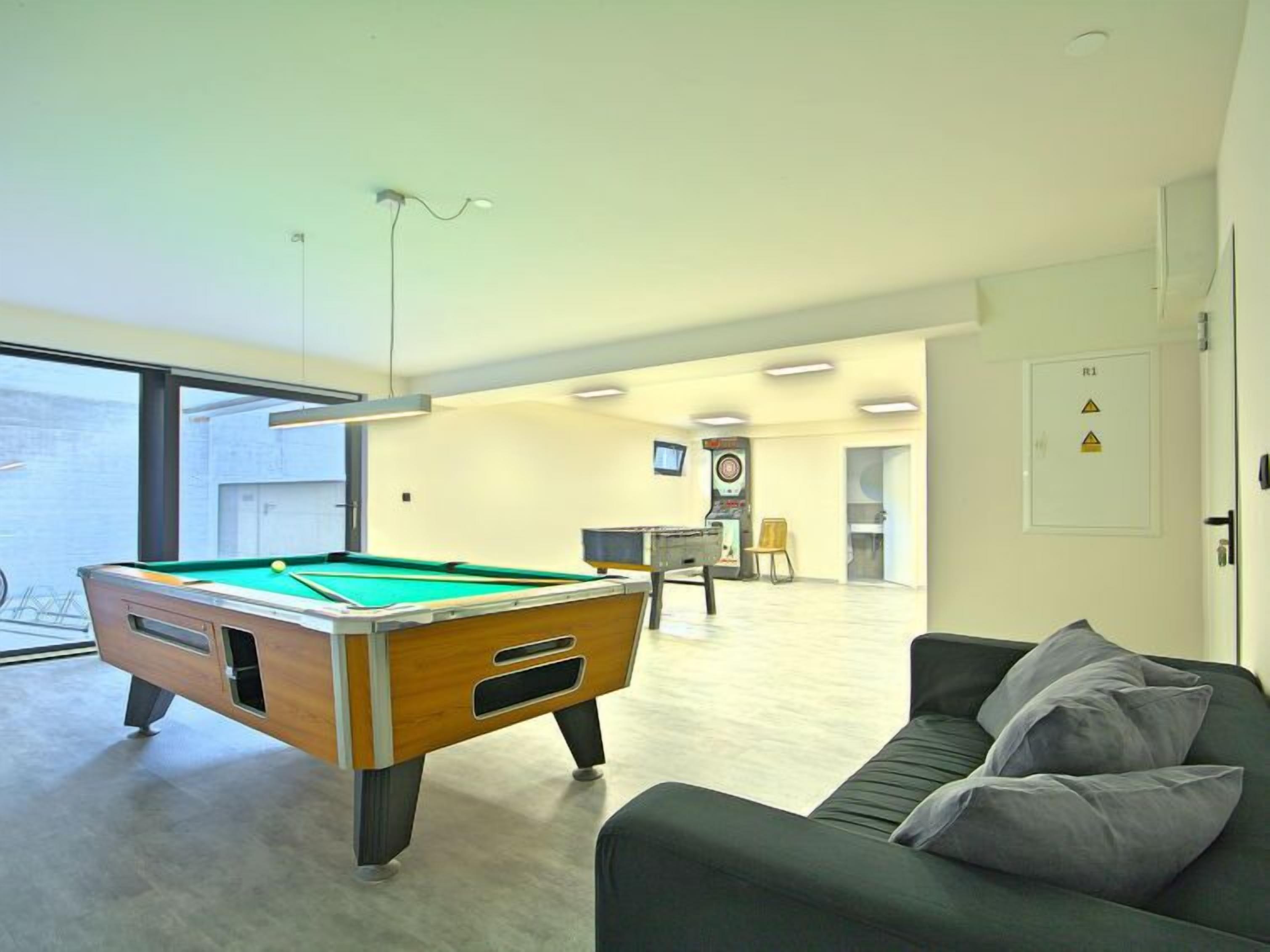 A modern living room with a pool table, a sofa, and a small table with a chair.