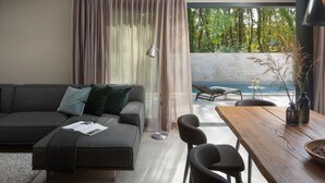 Una sala moderna con un sofá gris, una mesa de comedor de madera y vista a una piscina.