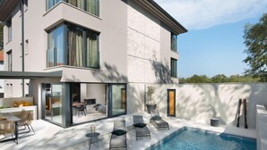 Una casa moderna de dos pisos con piscina, mobiliario exterior y un ventanal grande con vista a la piscina.