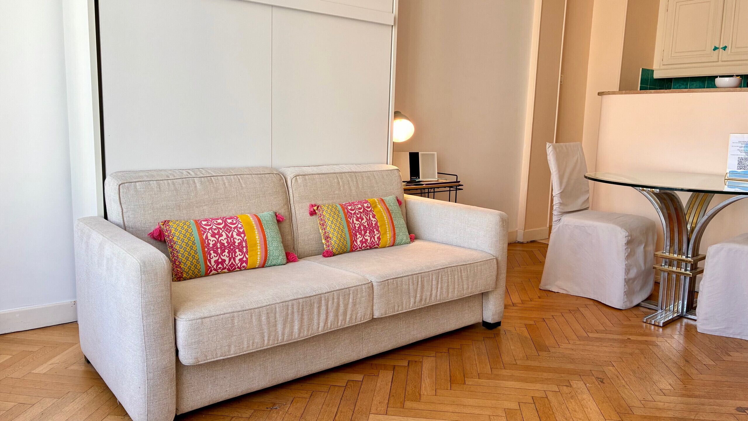 Un salon moderne avec un canapé de couleur claire, deux coussins décoratifs à motifs, une petite table d’appoint et une table basse avec un plateau en verre.