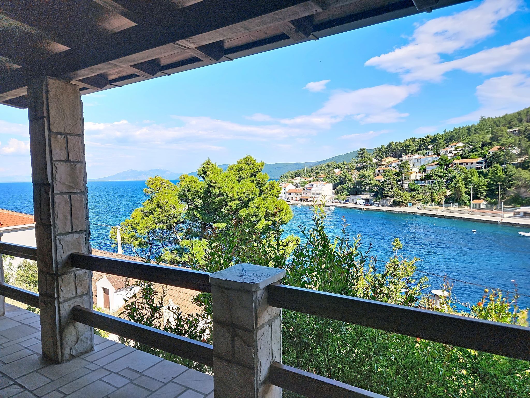 A coastal view with a stone railing, a clear sky, and buildings along the shoreline.