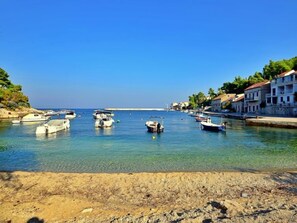 A coastal marina with several boats docked, clear blue water, and buildings along the shore.