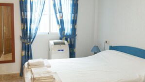 A hotel room with a bed, a window with curtains, an air conditioning unit, and a lamp.