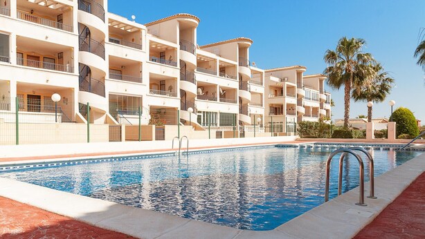 A multi-story hotel with balconies, a swimming pool, and palm trees.