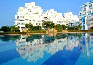 Um hotel moderno com vários edifícios brancos, piscina e céu azul límpido.