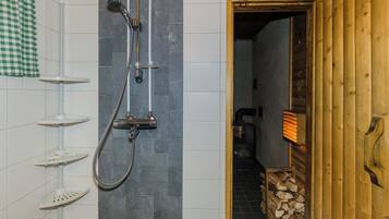 Un baño con ducha, paredes de azulejos y una puerta de madera que da a otra habitación.