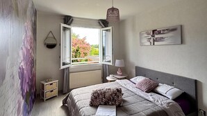 A bedroom with a bed, a window, a lamp, and a wall art piece.