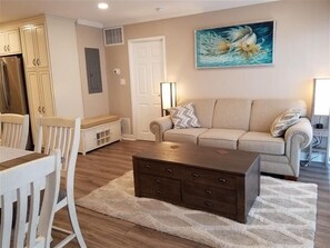 Uma sala de estar com um sofá bege, uma mesa de centro de madeira e um quadro de um peixe na parede.