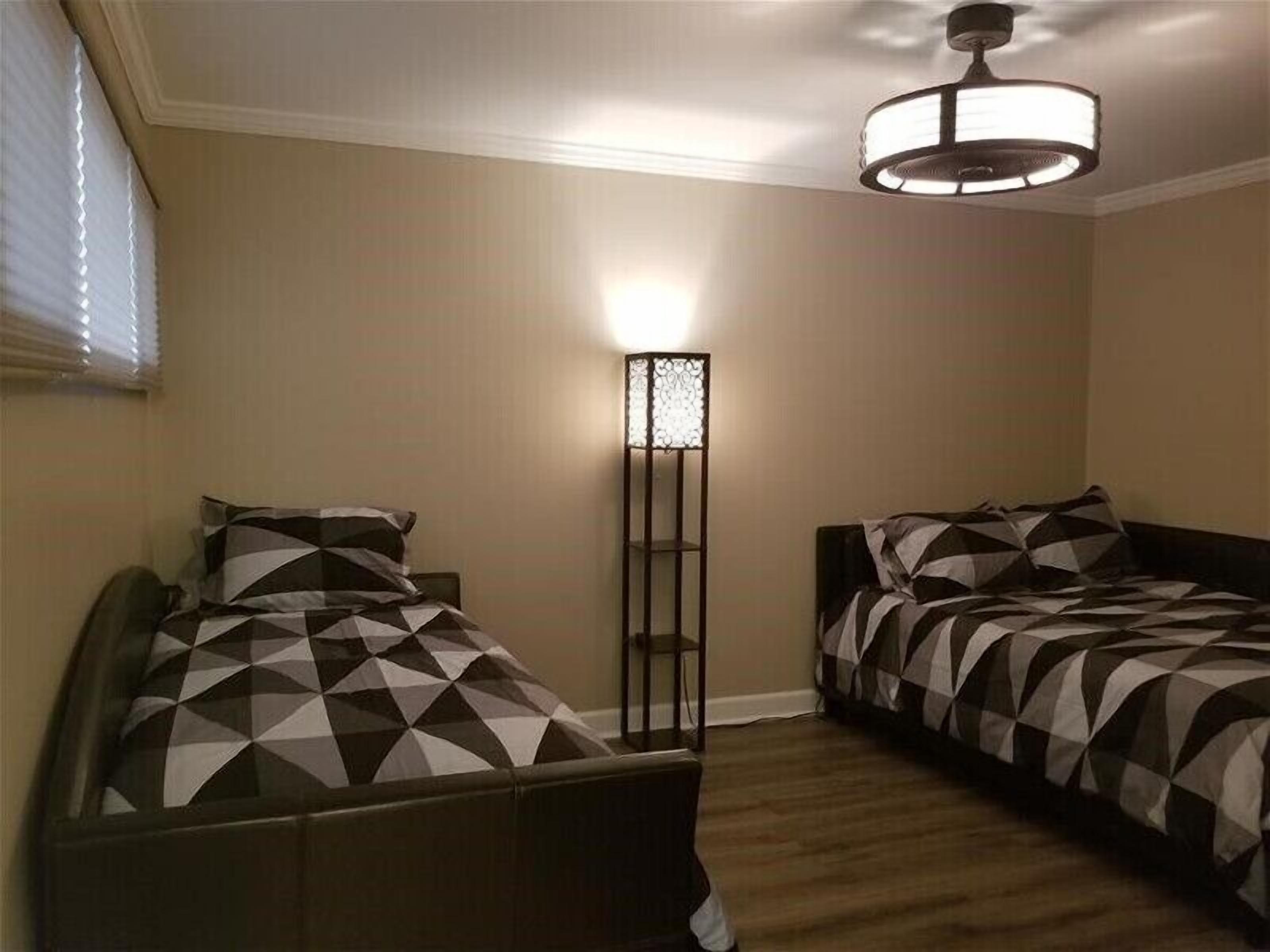 A bedroom with two beds, a floor lamp, and a ceiling light fixture.