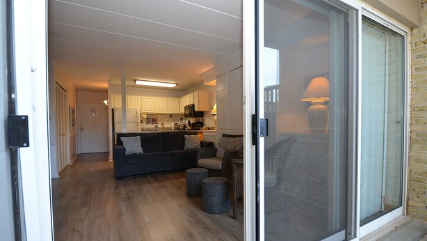 An open sliding door leading to a living room with a sofa, ottomans, and a kitchen area in the background. - 2 Bedrooms & 1 Bath in Rehoboth Beach, DE Ocean Block (Rehoboth Beach)