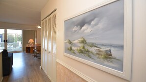 A hallway with a large framed painting of a beach scene, a wooden bench, and a table with chairs. - 2 Bedrooms & 1 Bath in Rehoboth Beach, DE Ocean Block (Rehoboth Beach)
