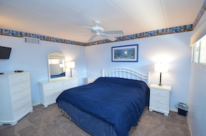 A bedroom with a bed, two nightstands, a ceiling fan, a TV, a mirror, and a picture on the wall.