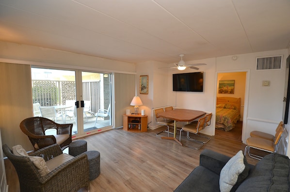 A room with a dining table, chairs, a sofa, a lamp, and a television.
