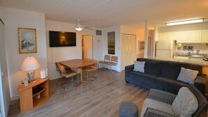 A living room with a sofa, a dining table with chairs, a TV mounted on the wall, and a kitchen area with cabinets and a refrigerator. - 2 Bedrooms & 1 Bath in Rehoboth Beach, DE Ocean Block (Rehoboth Beach)