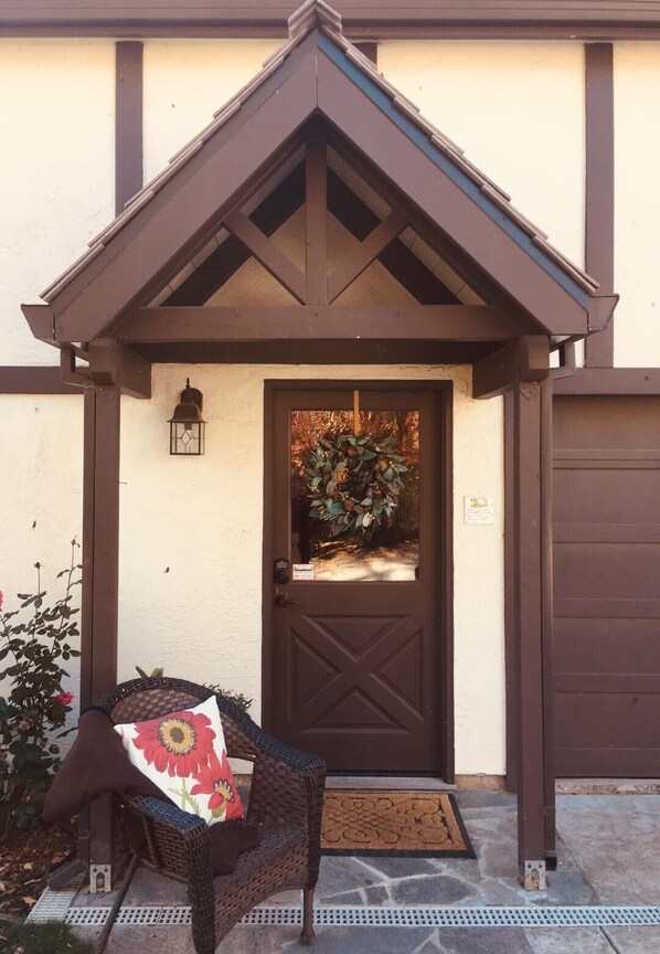 A brown door with a decorative wreath, a wicker chair with a floral cushion, and a small lantern above the door. - Welcome to Sunset Hills Ranch! (Sutter Creek)