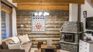 A cozy log cabin interior with a stone fireplace, a sofa, a coffee table, and a television.
