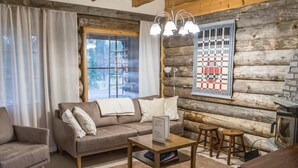 A cozy living room with a sofa, armchair, and coffee table, featuring a rustic log wall and a quilted artwork.
