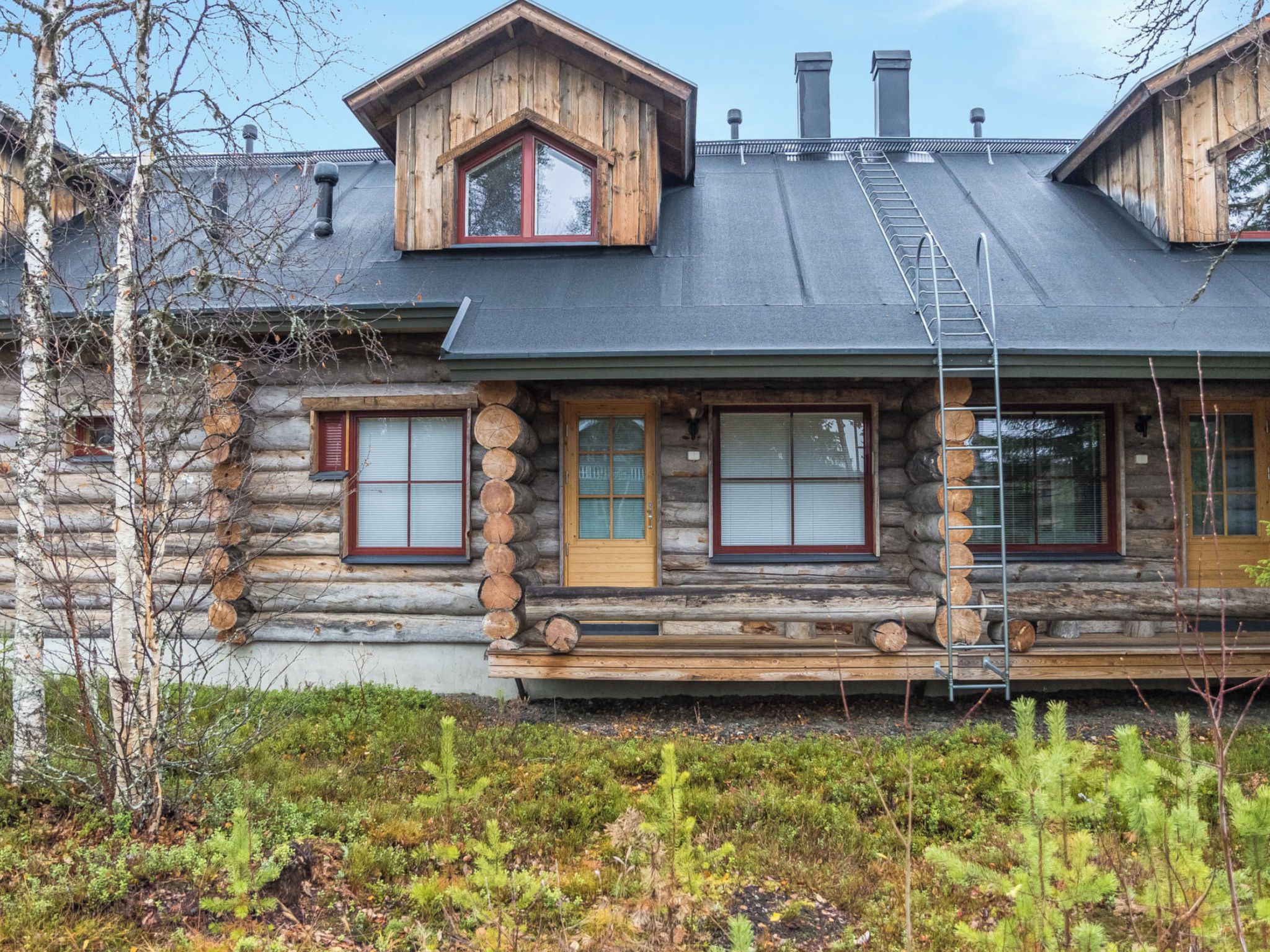 A log cabin with a steeply pitched roof, a front porch with a wooden bench, and a visible chimney.
