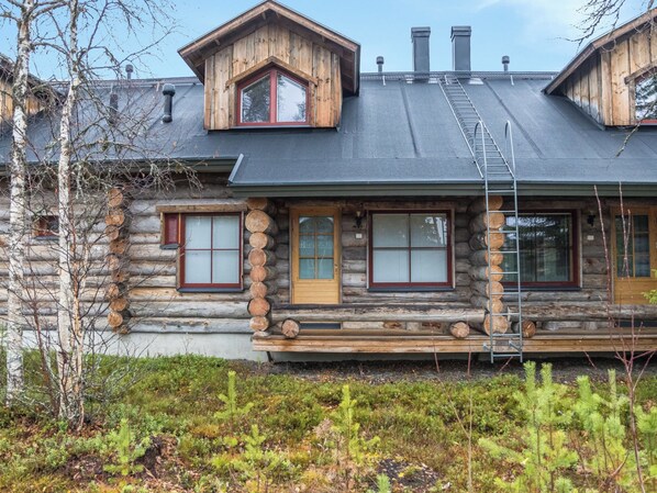 A log cabin with a steeply pitched roof, a front porch with a wooden bench, and a visible chimney.