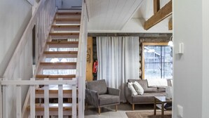 A staircase leading to an upper floor, a living room with two sofas and a coffee table, and a window with blinds.