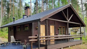 Una cabaña rústica con terraza de madera, chimenea y porche con mobiliario.