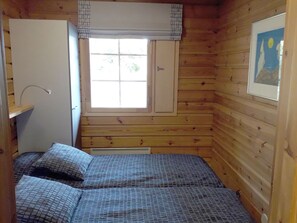 A small room with wooden walls, a window with curtains, a bed with patterned bedding, and a radiator under the window. - Vacation home Aili by Interhome (Padasjoki)