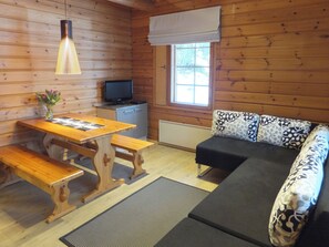 A wooden cabin interior with a wooden table, benches, a sofa with patterned cushions, a television, and a window with a view of greenery. - Vacation home Aili by Interhome (Padasjoki)