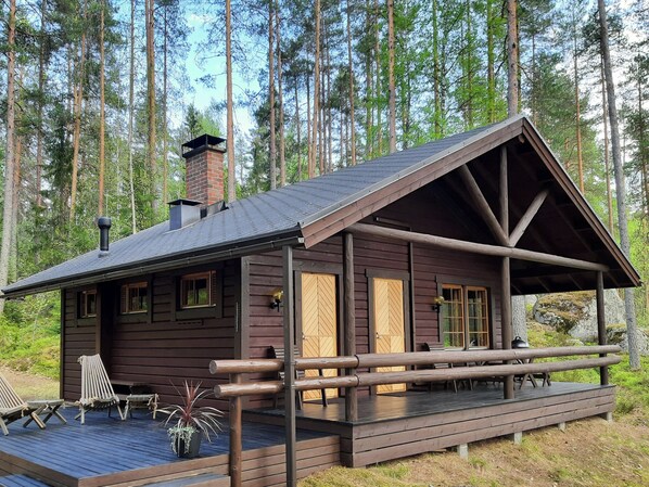 A cabin with a wooden deck, a covered porch, and a chimney.