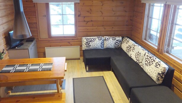 Un interior de cabaña acogedor, con paredes de madera, un sofá, una mesa y una lámpara.