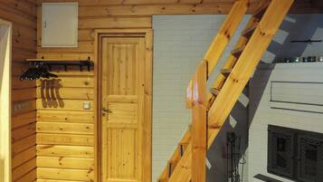 A wooden cabin interior with a wooden door, a staircase, and a fireplace.