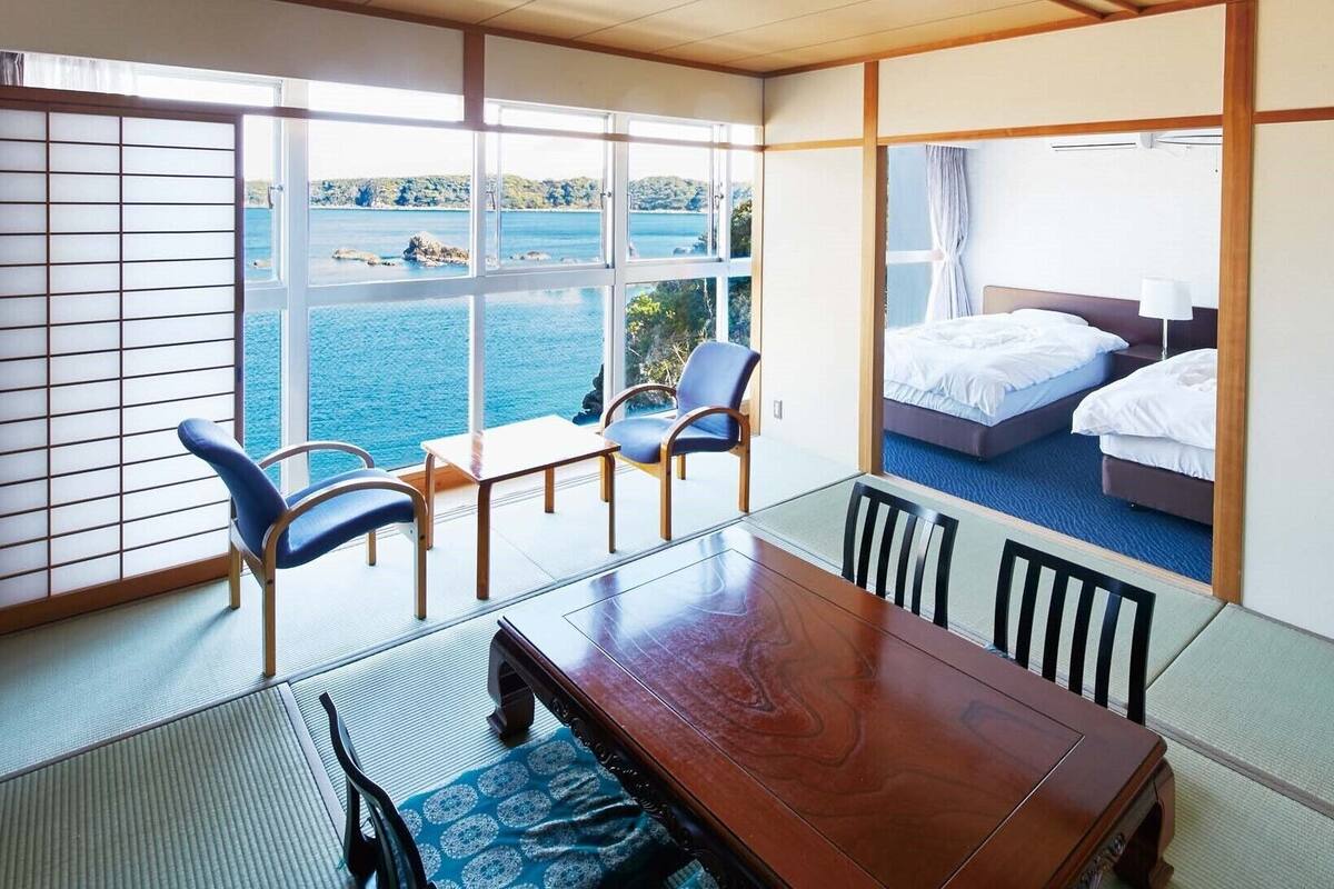 Une pièce comprenant une table à manger, des chaises, un lit et donnant sur la mer.