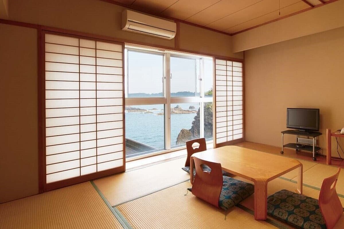 Une pièce de style japonais traditionnel, avec un sol recouvert de tatamis, une porte coulissante donnant sur la mer, une télévision et une petite table.