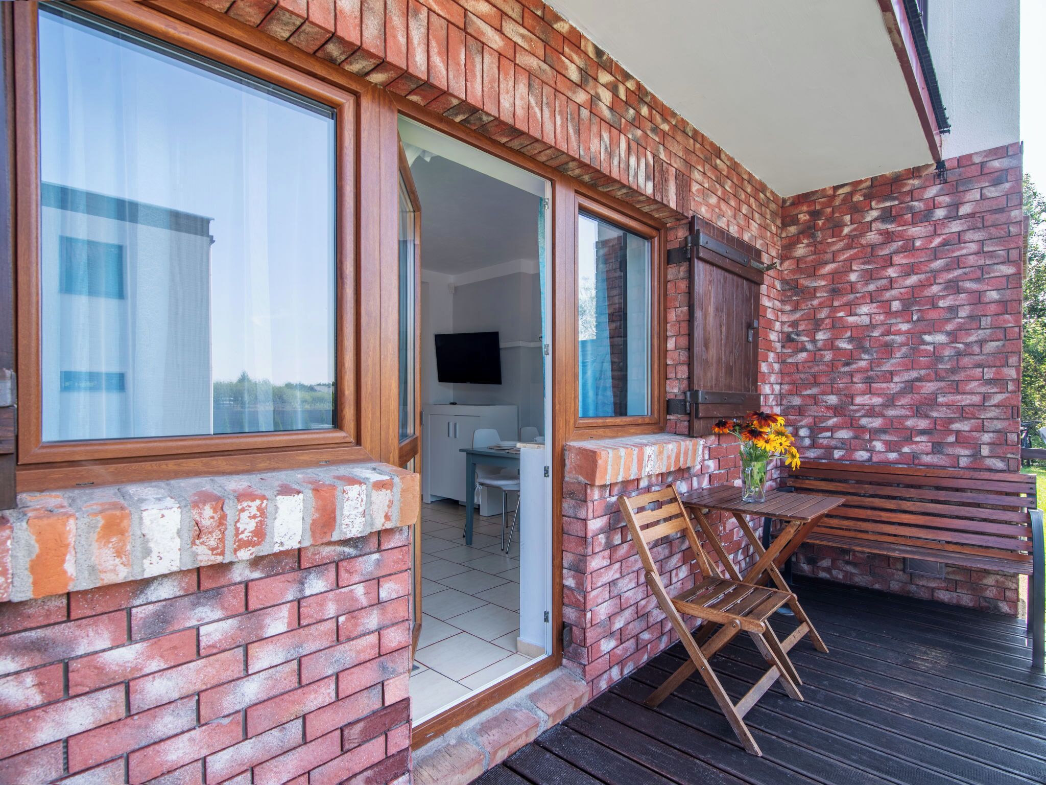 A brick exterior with a wooden deck, a table with chairs, and a bench.