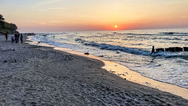 A beach with a sunset, waves, and people walking along the shore. - Nostalgia by Interhome (Mielno)