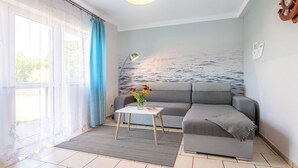 A modern living room with a grey sofa, a small table with a vase of flowers, and a wall mural of the sea. - Nostalgia by Interhome (Mielno)