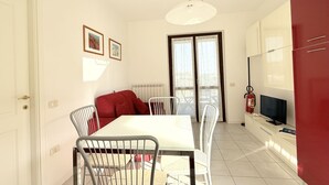 Un comedor con una mesa y sillas blancas, un sofá rojo, un televisor y un extintor.