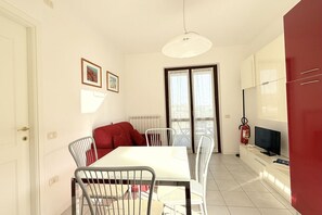 Un comedor con una mesa y sillas blancas, un sofá rojo, un televisor y un extintor.