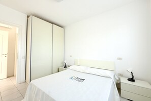A hotel room with a bed, a nightstand, a lamp, a wardrobe, and a door. - N059 - Numana, new two-room apartment with terrace (Maratta)