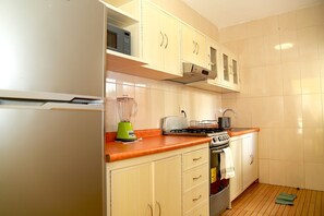 Compact kitchen with modern design, featuring white and light wood cabinetry, and equipped with a refrigerator, microwave, toaster, gas stove, blender, and kettle.