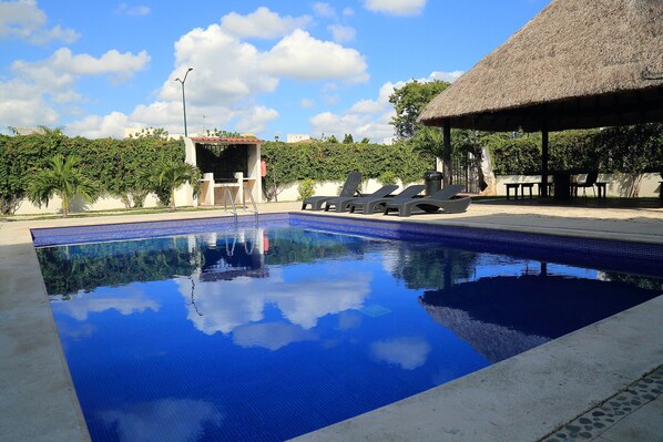 Relax by the serene pool surrounded by lush greenery and a rustic gazebo.