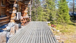 A log cabin with a wooden deck, outdoor seating, and a large tree in the background.