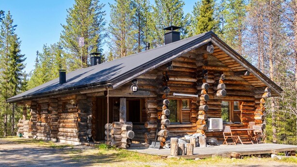 A log cabin with a porch, a chimney, and a deck with chairs.
