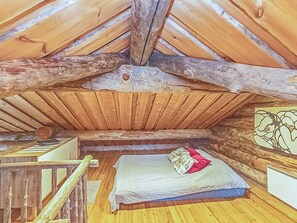 A rustic attic bedroom with a sloped ceiling, wooden beams, a bed with a quilt, and a small table. - Rukaveska 4a by Interhome (Kuusamo)