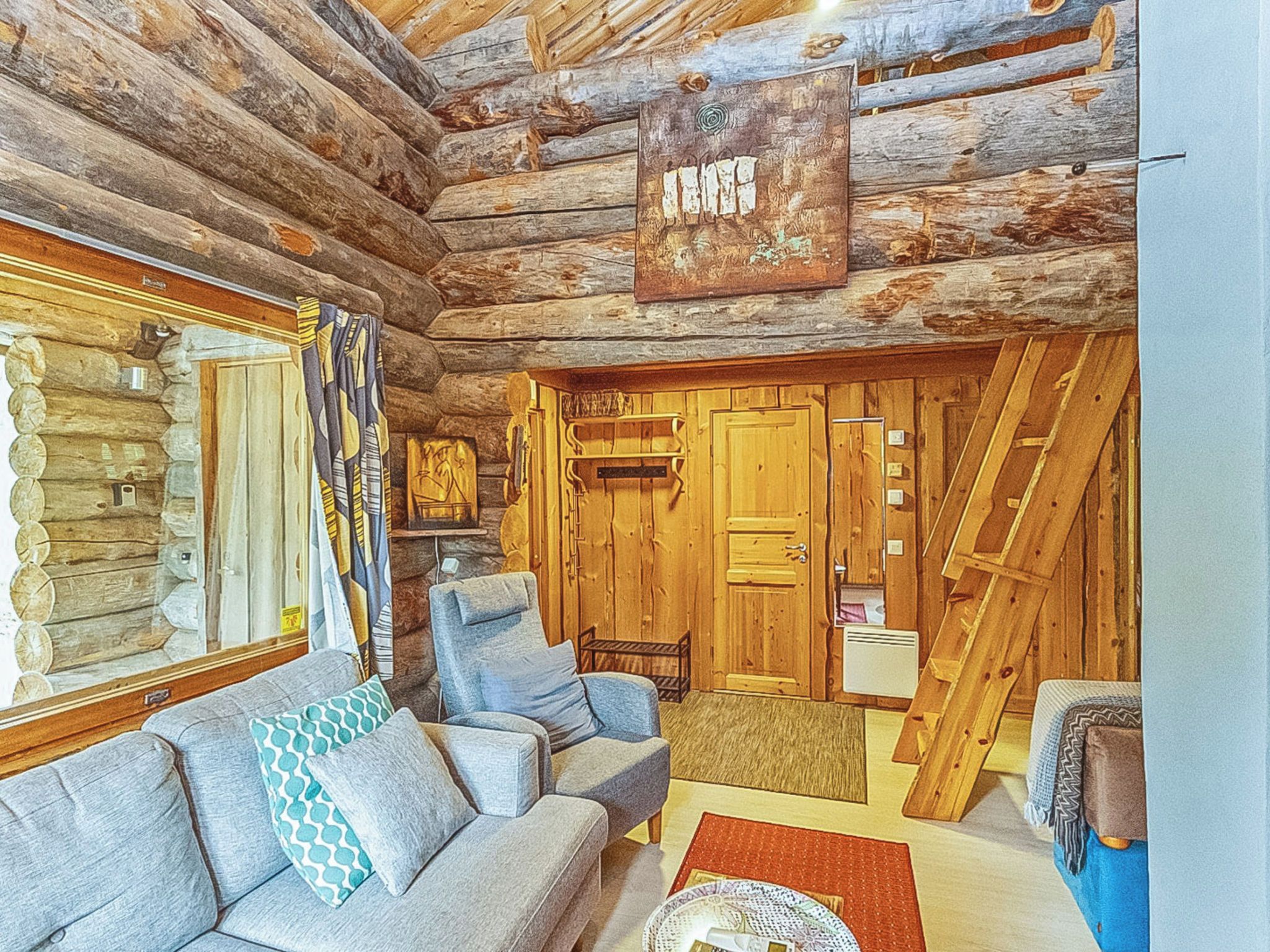 Interior de una cabaña de troncos con un sofá, un sillón, una chimenea y una escalera de madera.
