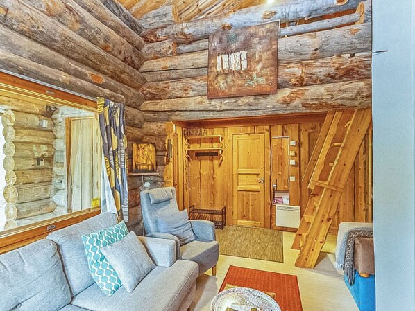 A log cabin interior with a sofa, a chair, a fireplace, and a wooden staircase.